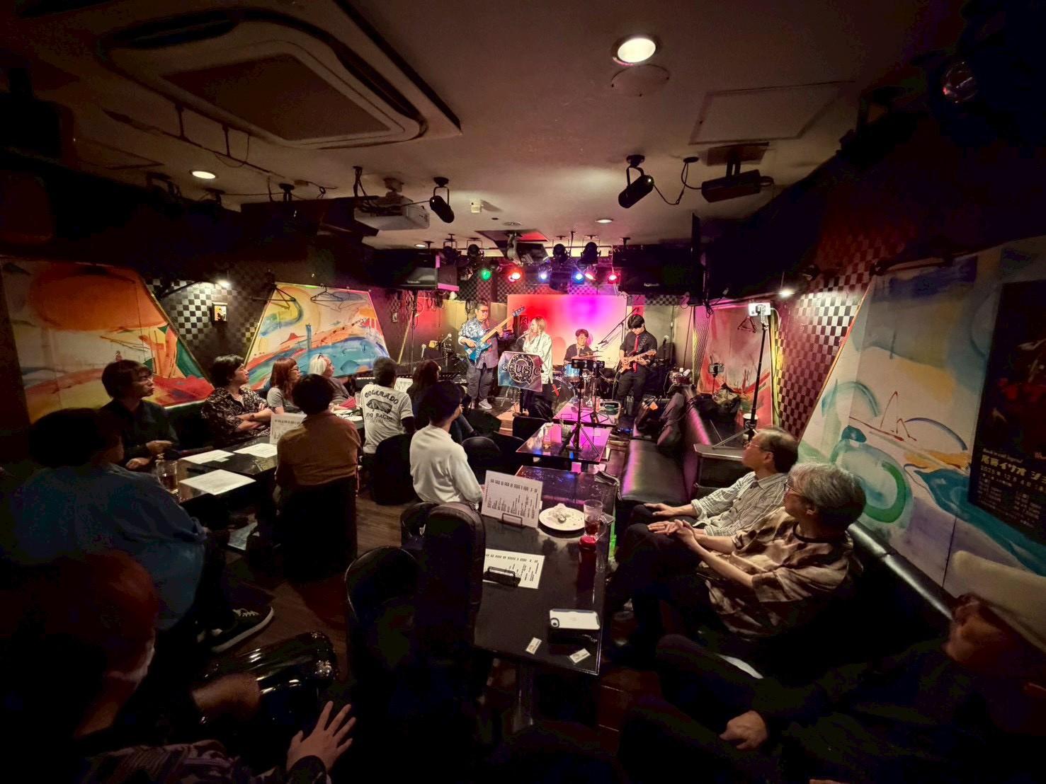 客席から見たライブハウス全景。ステージ奥でQEUSICが演奏し、テーブル席の客が聴いている