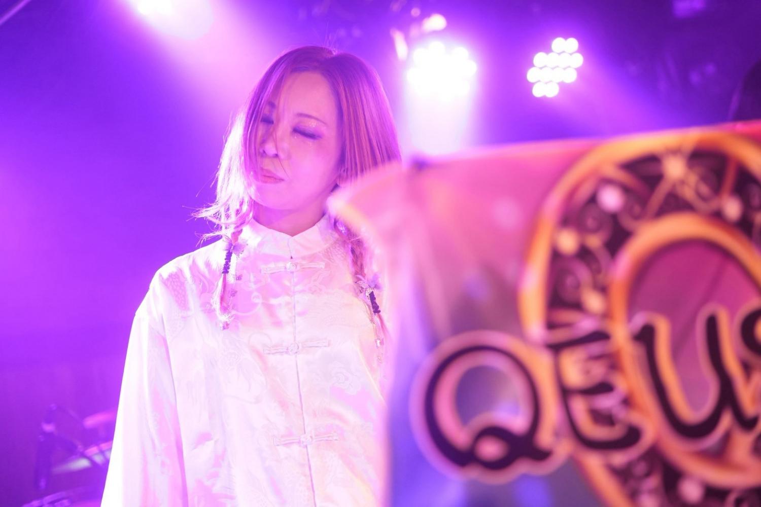 QEUSIC旗の横、紫の光の中で目を閉じる JUN