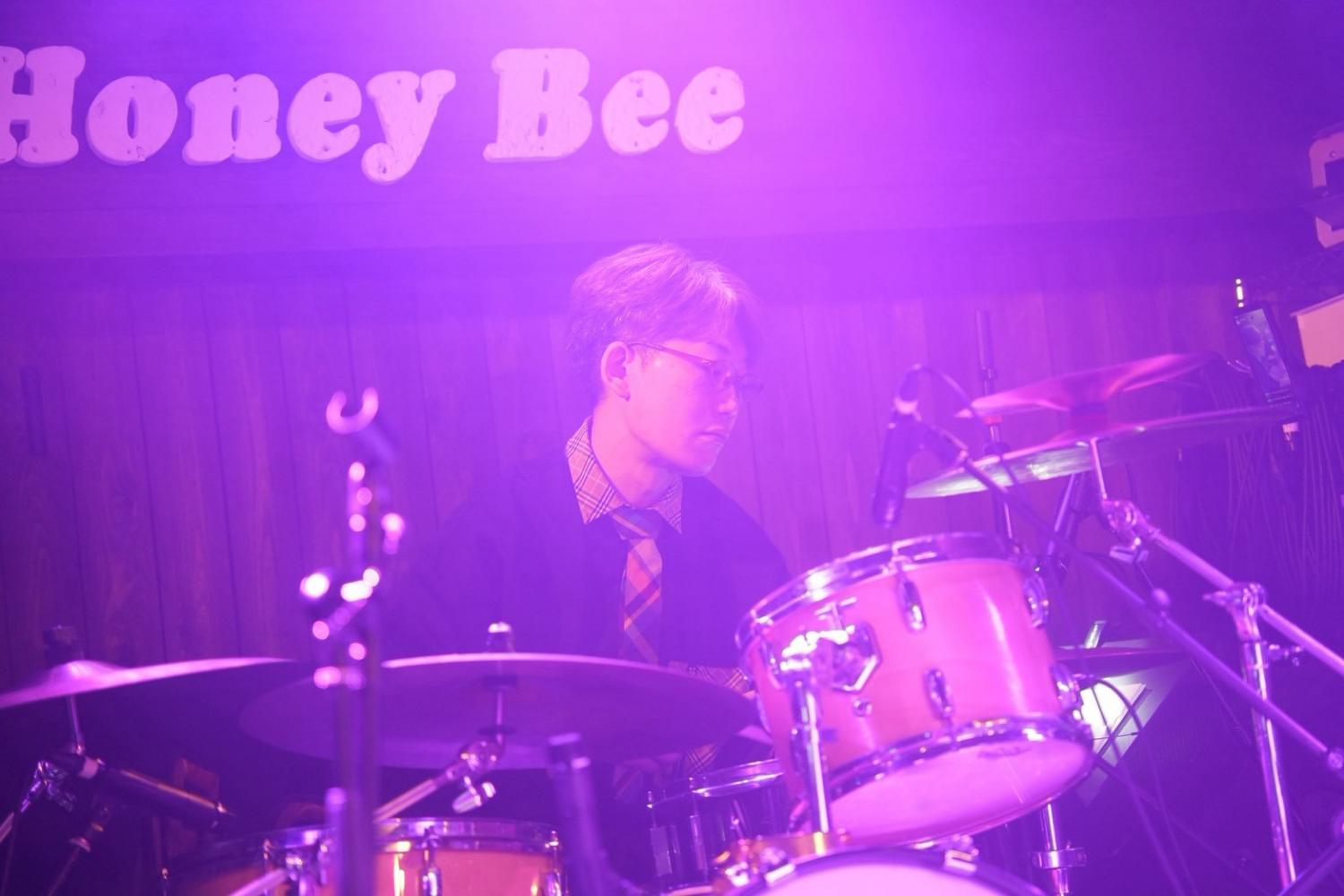 紫のHoney Bee。チェックのネクタイでドラムを叩く まこ