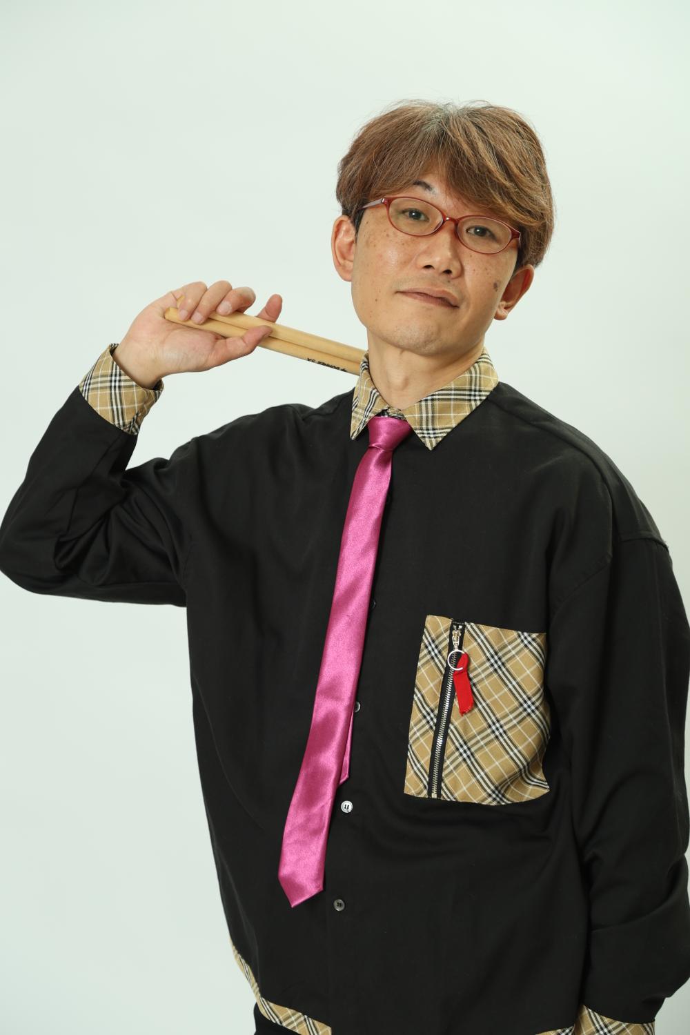 QEUSIC ドラム まこ。白い背景、ピンクのネクタイ、スティックを肩に