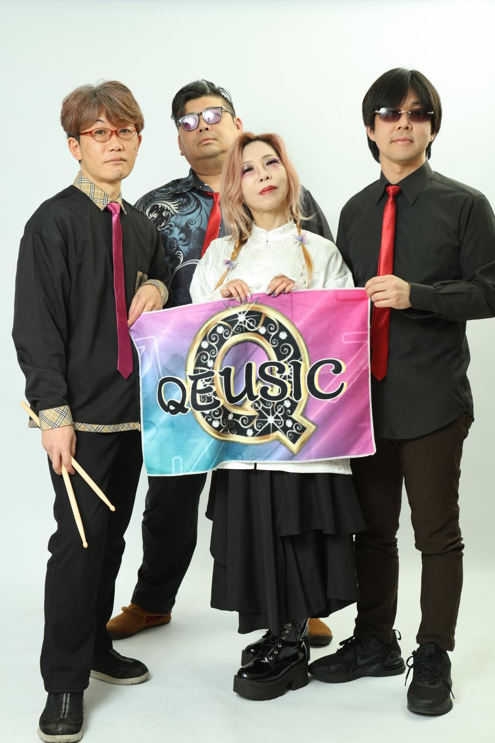 白い背景、QEUSIC旗を掲げる4人。左からまこ、のすけ、JUN、みっくん