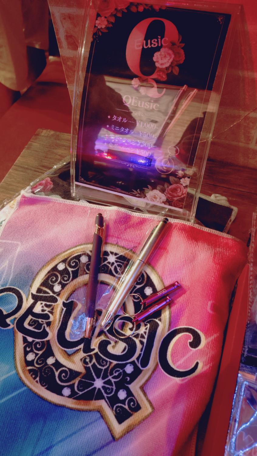 QEUSICのタオル、ボールペン、ホイッスルと物販ポップ。タオル¥1000