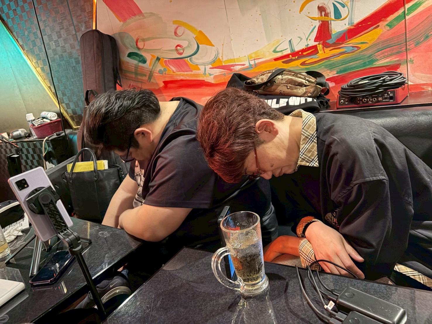 テーブルに突っ伏す のすけ と まこ。ビールジョッキとスマホ